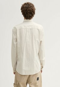 Hellbeiges Langarmhemd mit dezentem Karomuster, Knopfmanschetten und geradem Saum. Hergestellt aus einem strukturierten Stoff mit glatter Oberfläche.