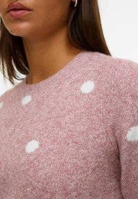 Maglione rosa a maglia con pois bianchi, con scollatura rotonda e texture morbida. Ripresa dall'alto che si concentra sulla zona del petto.