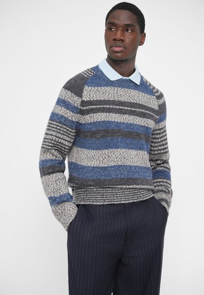 Πλεκτό πουλόβερ με στρογγυλή λαιμόκοψη, διακοσμημένο με ρίγες σε γκρι, μπλε και λευκό χρώμα. Συνδυάζεται με ανοιχτό μπλε πουκάμισο με γιακά από κάτω.