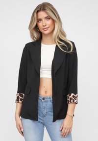 Svart blazer med hakket krage, med leopardmønsterdetaljer på mansjettene. Laget av glatt stoff, designet med to fremre lommer.