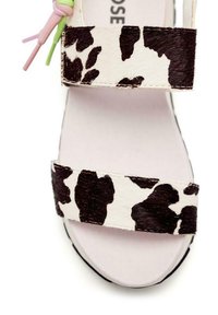 Chanclas con estampado de vaca que presentan un material suave y texturizado con patrones en blanco y negro, doble tirante y acentos en tonos pastel.