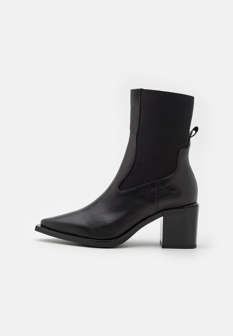 Bottine en cuir noir avec bout pointu, panneaux latéraux élastiques, languette à l'arrière et talon carré sur fond blanc.
