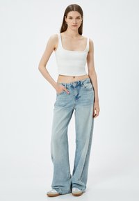 Witte geribbelde cropped top met brede bandjes, gecombineerd met lichtblauwe, losse denim jeans. De outfit heeft een ontspannen ontwerp en minimale details.