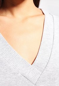 Graues geripptes V-Ausschnitt-Top mit tiefem Ausschnitt und glatter Textur, mit Fokus auf Kragen- und Schulterbereich.