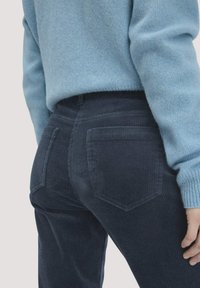 Donker marineblauwe corduroy broek met kenmerkende ribbels, voorzien van twee achterzakken en een middelhoge taille, gecombineerd met een lichtblauwe gebreide trui.