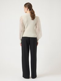 Cream ribbed sweater with sheer, puffed sleeves; paired with high-waisted black trousers. Simple design with a fitted bodice and flowing, textured sleeves.