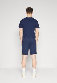 Ensemble en coton bleu marine comprenant un t-shirt et un short, avec un col blanc, des rayures latérales dorées, et des chaussettes blanches à hauteur de cheville avec des chaussures décontractées.