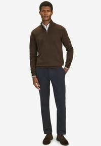 Brauner Strickpullover mit Reißverschlusskragen, kombiniert mit dunkelblauen Hosen. Braune Wildlederschuhe runden das Outfit ab. Einfaches Design; keine Muster oder Akzente.