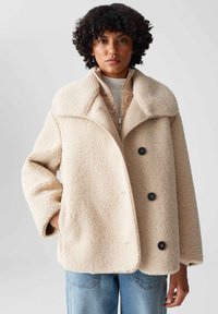 Beige Übergröße-Jacke aus strukturiertem Fleece. Mit großen Revers, einem Reißverschluss und zwei schwarzen Knöpfen. Lockere Passform mit Seitentaschen.