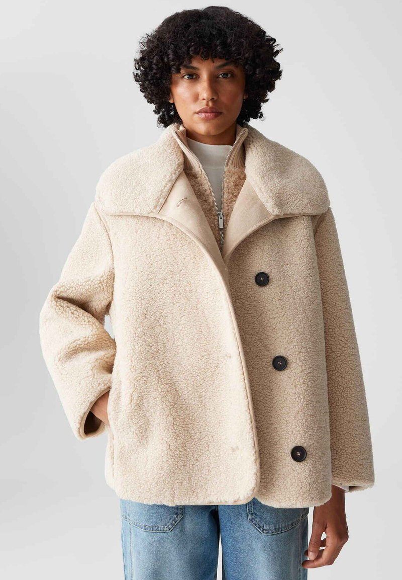 Beige Übergröße-Jacke aus strukturiertem Fleece. Mit großen Revers, einem Reißverschluss und zwei schwarzen Knöpfen. Lockere Passform mit Seitentaschen.