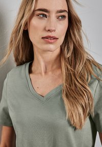 Světle zelené tričko s krátkým rukávem a výstřihem do V, vyrobené z měkké látky, s hladkým povrchem a jednoduchým designem. Žádné viditelné vzory ani akcenty.