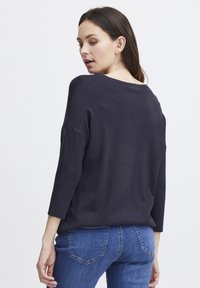 Jūras karaflotes adīta džempera brīvs piegriezums, apaļš kakls un trīs ceturtdaļu piedurknes. Materiāls šķiet mīksts, ar minimālām tekstūras detaļām.