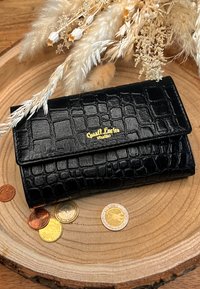 Portafoglio nero in pelle con stampa a coccodrillo, con una patta e logo dorato. Monete sparse su una superficie di legno. Texture liscia.