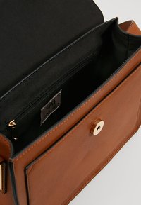 Brun läderväska med axelrem, guldknäppning, svart innerfoder och en innerficka med dragkedja. Märkesetikett synlig inuti.