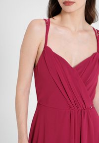 Mauve Kleid mit V-Ausschnitt und gefaltetem Oberteil. Es hat dünne Träger mit metallischen Akzenten und einen glatten, fließenden Stoff.