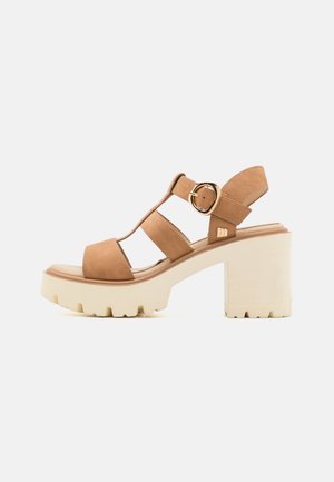 Des sandales à plateforme en suède tan présentent une conception à trois brides, une boucle réglable et un talon épais de couleur crème avec une semelle texturée.