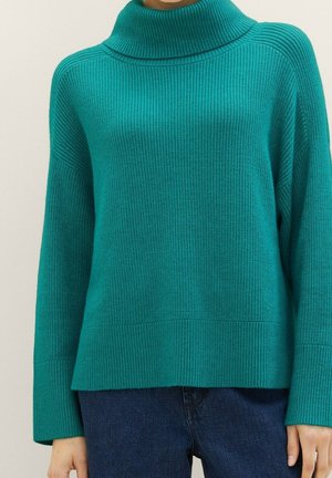 Pull col roulé côtelé couleur sarcelle à manches longues, porté avec un jean bleu foncé, visible des épaules jusqu'aux hanches.