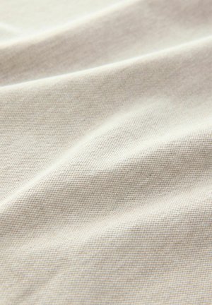 Naturalny materiał tekstylny w jasnobeżowym kolorze, z teksturowaną powierzchnią, która prezentuje delikatne sploty i zagięcia, ukazując miękkość i elastyczność.