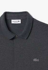 Mörkgrå piké i bomullsmaterial, normal passform, med klassisk krage, tvåknappsknäppning och broderad Lacoste-logga på vänster bröst.