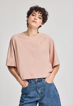 Lyserød cropped t-shirt lavet af blødt stof, med korte raglanærmer og en diskret logo detalje på fronten. Sammen med højtaljede denimbukser.