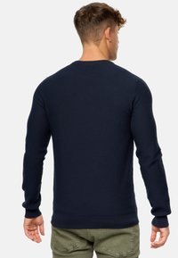 Marineblå strikket sweater med struktureret mønster, rund halsudskæring og ribbede manchetter. Bagfra ses det tætsiddende design med en lige kant.