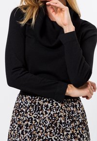 Czarny sweter z dekoltem w kształcie kołnierza, z długimi rękawami, połączony z plisowaną spódnicą w beżowo-brązowy wzór lamparta na ciemnym tle.