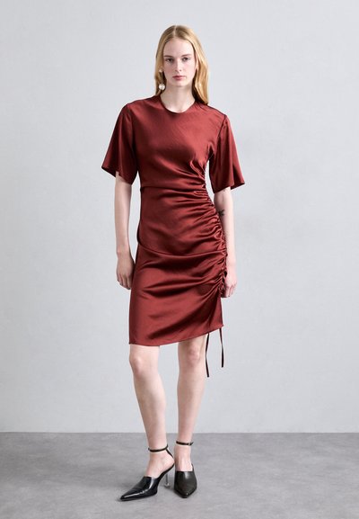 Reddish-brown satin dress with short sleeves and side ruching, featuring a tapered hemline. Model wears black pointed-toe heels.