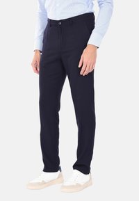 Pantaloni blu navy con design a pantaloni piatti, realizzati in tessuto leggero, dotati di chiusura con bottone e tasche laterali, abbinati a sneakers bianche.