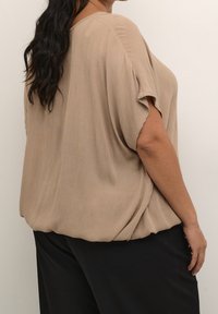 Beige, losse blouse van een textuurstof, korte mouwen en een oversized pasvorm, gecombineerd met zwarte broek.