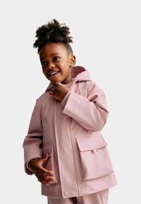 Růžová voděodolná bunda s kapucí, vybavená dvěma předními kapsami a hladkým, lesklým povrchem. Nosí ji dítě, které stojí s mírným úsměvem.