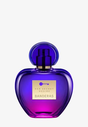 Flacon de parfum en forme de cœur avec un dégradé violet et rose, bouchon arrondi et étiquette dorée portant la mention "Her Secret Desire Banderas."