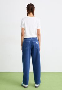 Relaxed-fit blauwe denim jeans met een rechte snit, voorzien van achterzakken, stiksels en een label. Gecombineerd met een wit t-shirt.