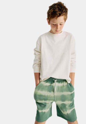 Camisa de manga larga color crema claro combinada con pantalones cortos de tie-dye verde que cuentan con una cinturilla elástica y bolsillos laterales.