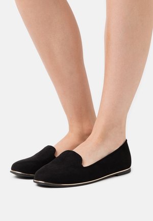 Schwarze Wildleder-Pantoletten mit runder Zehenpartie und niedrigem Profil. Mit einer goldenen Zierkante entlang der Sohle. Glatte Textur und minimalistisches Design.