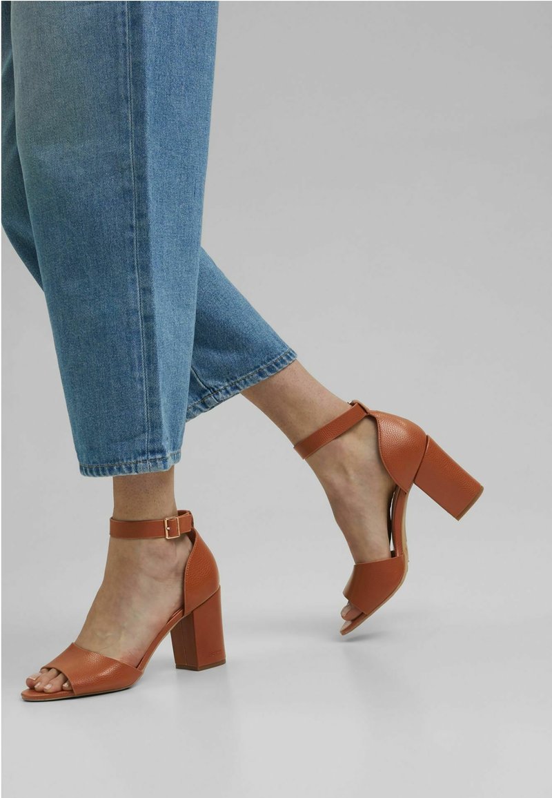 Sandales à talons hauts en cuir tan avec une bride de cheville, bout ouvert et un talon carré. Associées à un jean en denim bleu coupé.