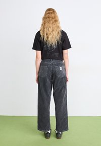Čierne skrátené tričko s grafickou potlačou, spárované s dark gray džínsami s širokými nohavicami. Čierne tenisky s textúrovanou podrážkou dotvárajú outfit.