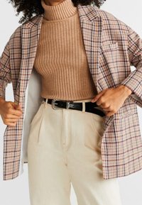 Karierter Blazer in Braun, Creme und Blau, über einem gerippten beigen Rollkragenpullover getragen. Creamfarbene Hochwasserhosen mit einem schwarzen Gürtel.