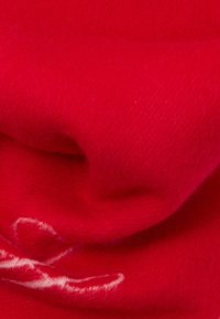 Raudona vilnos medžiaga su smulkia, švelnia tekstūra, su balta abstrakčia dizaino. Medžiaga atrodo lengva ir purus.