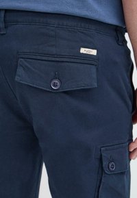 Marineblaue Cargo-Hosen aus strapazierfähigem Stoff, mit einer Gesäßtasche mit Knopfverschluss und einem kleinen aufgenähten Etikett.