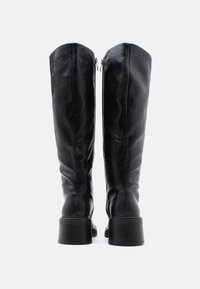 Μαύρες δερμάτινες μπότες έως το γόνατο με λεία υφή, διαθέτουν κάθετες ραφές και χοντρό τακούνι. Κλείσιμο με φερμουάρ στο πίσω μέρος.
