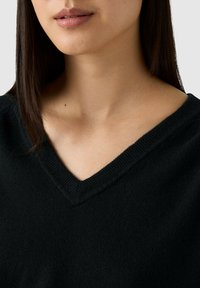 Maglione nero a V in materiale morbido, con un collo a costine e una texture liscia. Vista ravvicinata che mette in evidenza i dettagli del collo.
