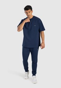 Námořnické modré bavlněné tričko a odpovídající teplákové kalhoty, s kulatým výstřihem, krátkými rukávy a nenápadným logem na hrudi. Bílé tenisky.