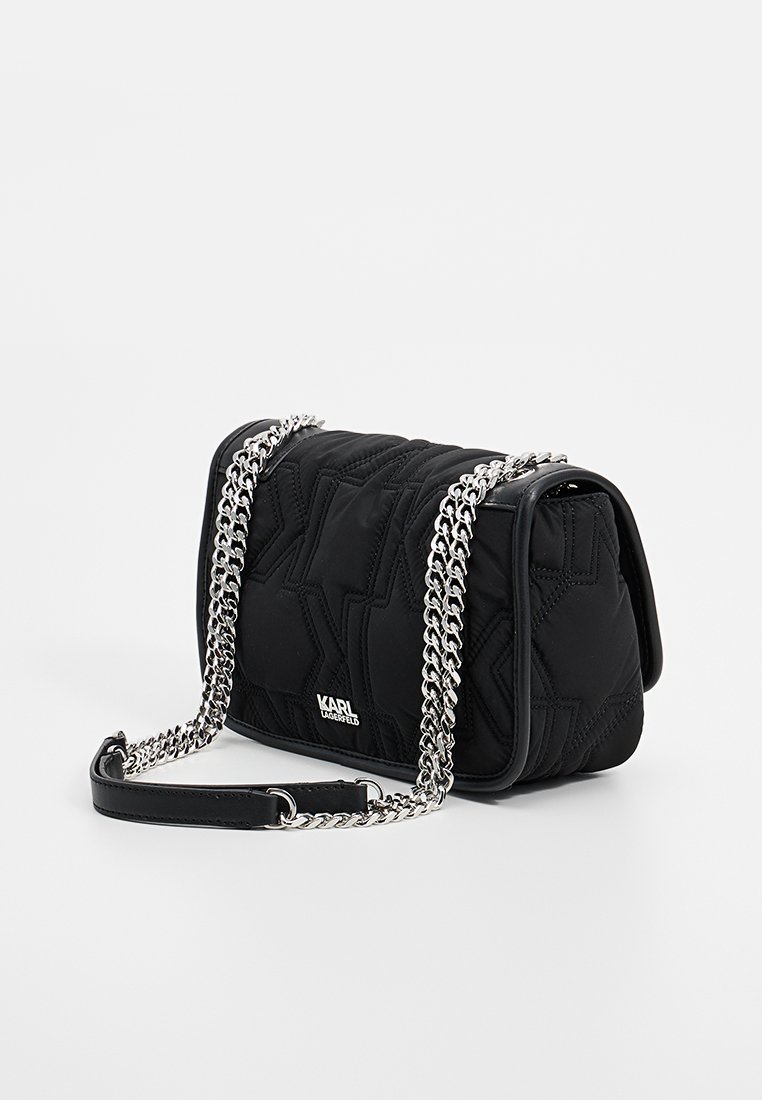 Sac à épaule noir matelassé avec une anse en chaîne argentée, doté d'un rabat à l'avant et d'un détail de logo. Format structuré avec une texture lisse.