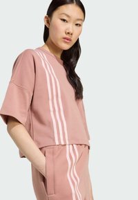 Ružový skrátený sweatshirt so širokými rukávmi, s tromi vertikálnymi bielymi pruhmi na boku. Mäkká, štruktúrovaná tkanina. Spárované s rovnakými nohavicami.