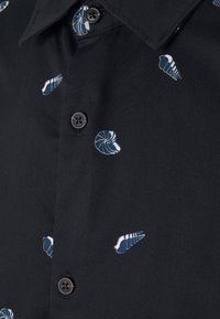 Maglietta nera con piccoli motivi a conchiglia bianchi e blu; colletto classico; tre bottoni visibili; texture liscia.