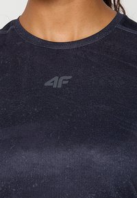 Ciemnoniebieska dopasowana koszulka sportowa z teksturowanej tkaniny, z małym szarym logo na klatce piersiowej oraz kontrastowym szwem na dekolcie.