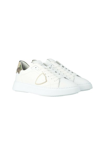 Een paar witte lage sneakers met vetersluiting, beige accenten aan de zijkanten en camouflagepatroon op de hiel.