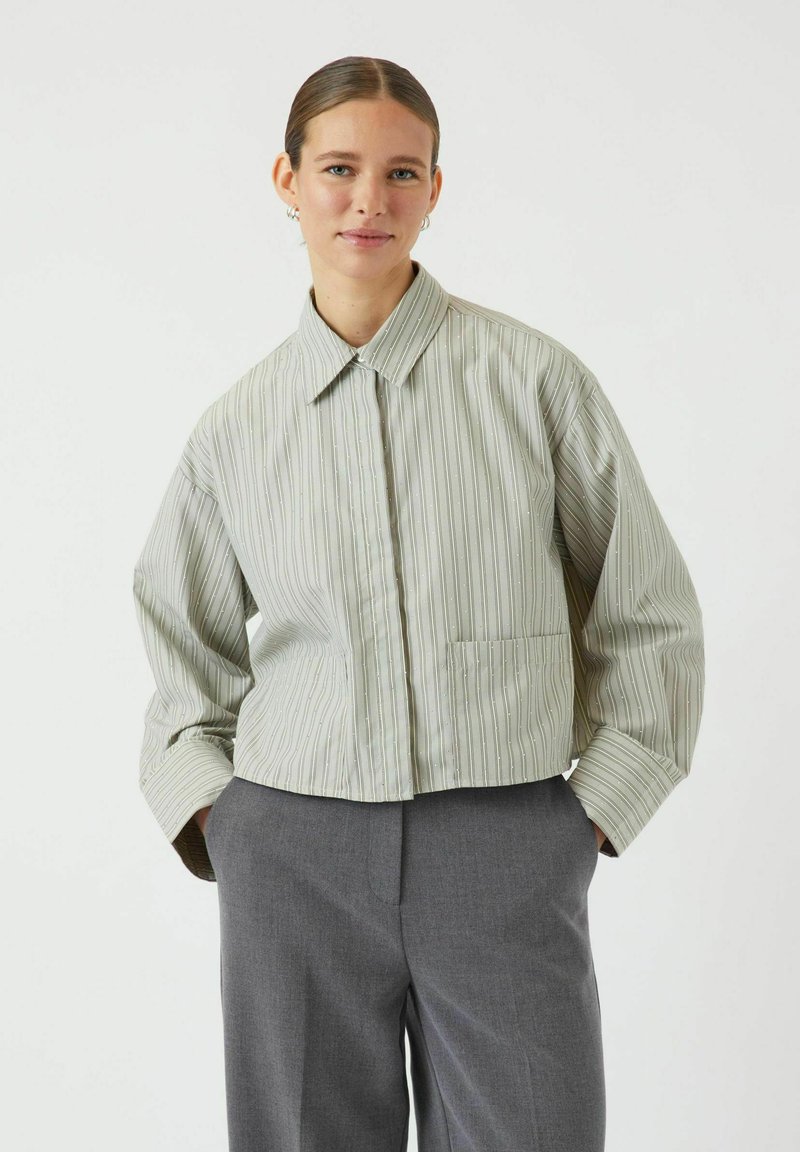 Afskåret jakke i grønne striber med knaplukning, spidse kraver, lange ærmer og en enkelt frontlomme. Glat tekstur med subtile detaljer.