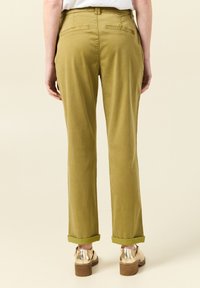 Pantaloni dritti verde oliva con orli arrotolati, due tasche posteriori e texture liscia. Indossati con scarpe con piattaforma dorate metallizzate.