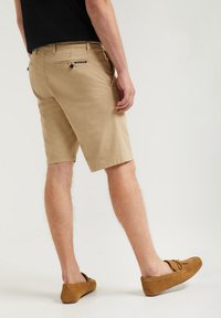 Khaki shorts i bomull med rak passform, med bakfickor, en logolapp och en uppvikt nederkant. Mocka slip-on skor är på fötterna.
